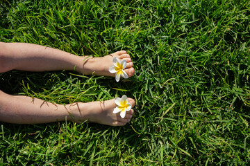 child bare feet with plumeria flowers between toes on green lawn . joy, cheerful positive...