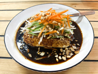 Tahu Telur, or egg beancurd, made of egg and beancurd deep fried together. It is served with shredded carrots and cucumber plus a sprinkle of peanuts served with sweet sauce.