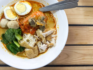 A bowl of curry noodles on wooden table.  Top view.