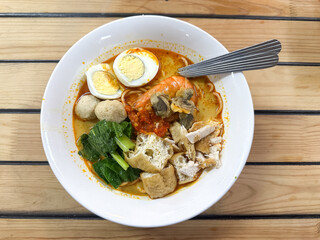 A bowl of curry noodles on wooden table.  Top view.