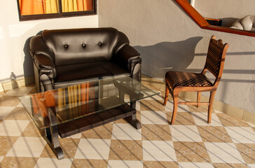 A black couch and a wooden chair sit on a tiled floor