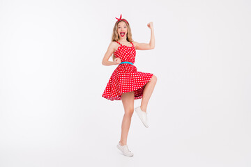 Young woman in red polka dot dress dancing joyfully on white background showcasing retro fashion...