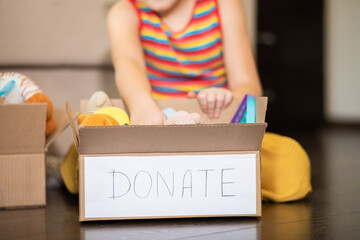 Cute teenager kid girl packing cuddly toys in the donation box at home.
