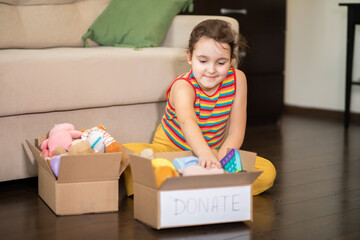 Cute teenager kid girl packing cuddly toys in the donation box at home.
