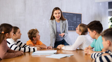 Inspired young female teacher working with preteens schoolgirls and schoolboys in modern classroom