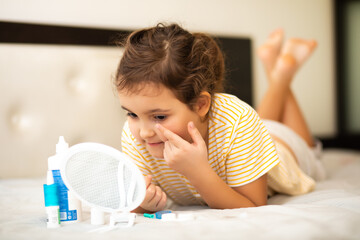 Cute little girl inserting contact lenses into her eye. Vision correction and ophthalmology for...