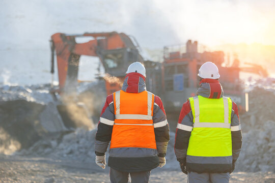 Open-pit coal mining with two male workers in high visibility gear, back view