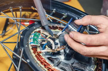 Bicycle mechanic holding soldering iron in his hands. Repairing electric motor of electric bicycle.