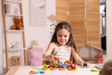 Fototapeta premium Motor skills development. Little girl playing with colorful wooden pieces at table indoors