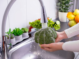 Woman hands washing fresh broccoli in the kitchen