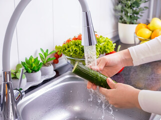 Woman hands washing a cucumber to prepare a fresh salad in the kitchen