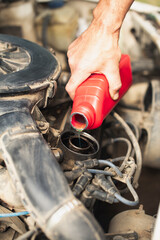 Close-up of a man's hand pouring a red container of motor oil into a car engine