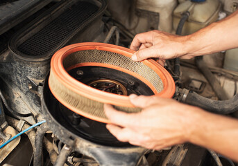 Close-up of a man&rsquo;s hands installing or removing a round air filter inside an old car 