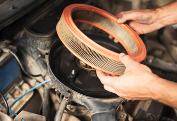 Close-up of a man&rsquo;s hands installing or removing a round air filter inside an old car