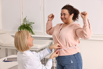 Happy woman lost weight. Smiling nutritionist measuring patient's waist with tape in clinic