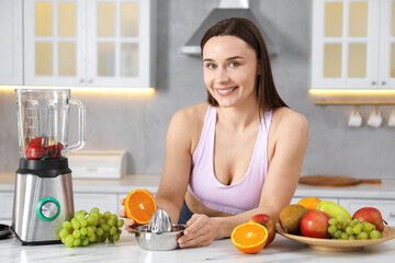 Woman in fitness clothes with orange and juicer making juice at white marble table indoors