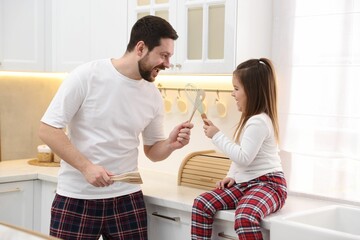 Obraz premium Happy father and his daughter wearing stylish pajamas playing with cookware in kitchen