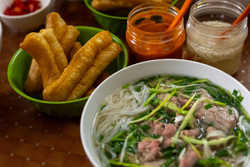 A bowl of beef pho sits surrounded by jars of condiments and fried dough in Hanoi, Vietnam on December 29, 2019