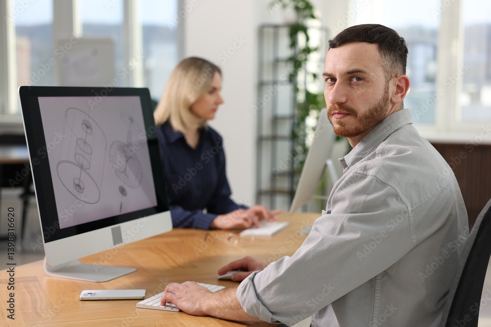 Poster engineer and his colleague working with computers at table in office