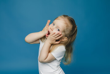 cute little girl 2-3 years old with blond hair looks at camera holds her face and is surprised.