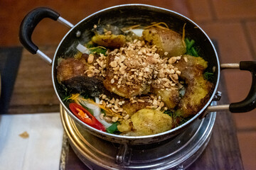 A close-up view of a Vietnamese rice noodle dish with grilled pork, peanuts, and fresh herbs served in a metal bowl at a restaurant in Ninh Binh, Vietnam, on December 26, 2019