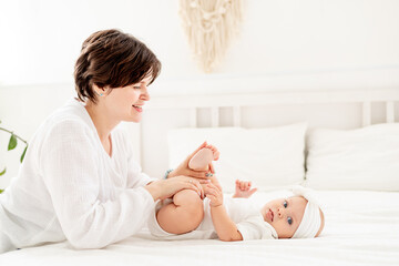 mom plays with baby's legs, happy family, mom with baby on the bed, mom hugs and kisses baby...