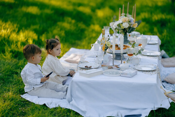 A young boy and a young girl are happily sitting at a table in the grass