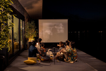 Group of friends watching outdoor movie at night on lakeside terrace