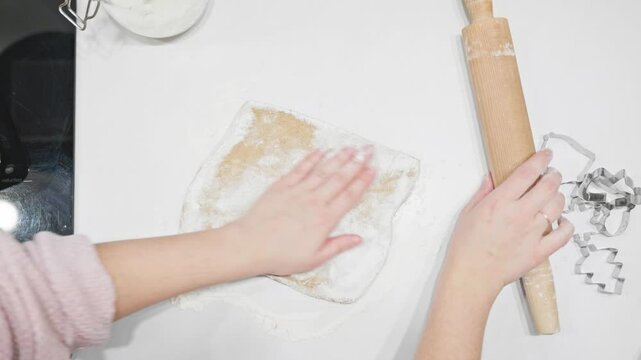 A close-up of hands rolling out dough for festive cookies on a floured countertop. Cookie cutters add charm to this cozy holiday baking experience