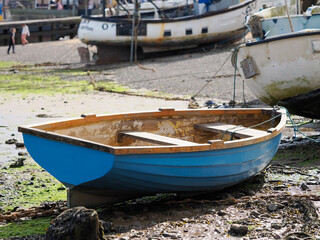 A small blue boat is sitting on the ground next to a larger boat