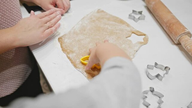 Hands carefully press cookie cutters into rolled gingerbread dough on a floured surface. Mom shows how to make cookies to her toddler. creativity and joy to holiday baking traditions.