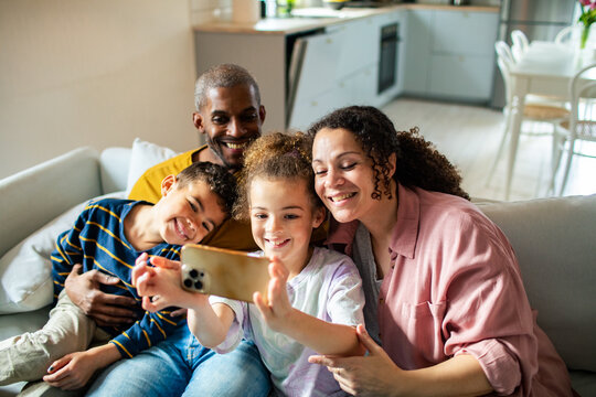 Happy mixed family taking group selfie at home on couch