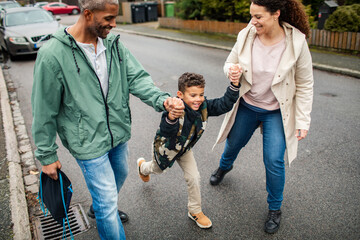 Happy parents walking to school with son on a rainy morning