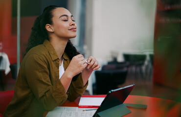Relaxed and carefree Latina digital nomad taking mindful break during remote work at stylish café....