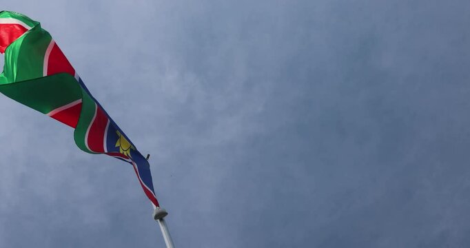 The National Flag of Namibia flutters in the wind. Great for news. Close-up. The Namibian flag against the blue sky. 4K video.