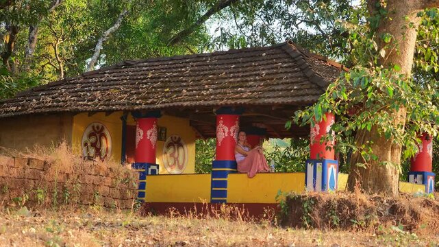 A woman relaxes in a colorful Indian ashram surrounded by lush forest.