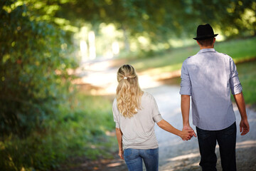 Back view of couple, hand holding and walking in park for love, bonding with care and support in...