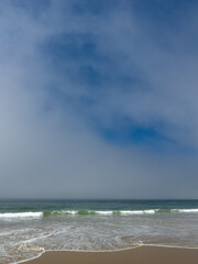 Sandy beach in the morning with a thick layer of marine clouds above the ocean in the horizon