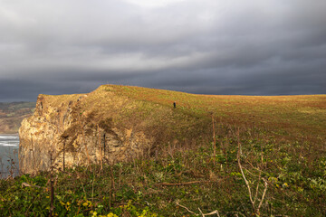 A small figure of a man walking against the background of mountains, sky and sea.