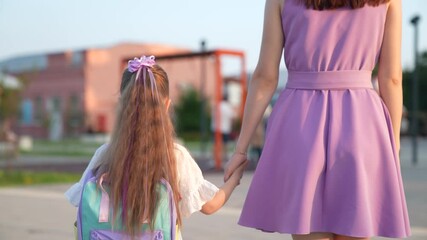 face smiling girl. mother leads girl with school backpack playground. happy family. girl walks park with swing. city playground. child girl smiling laughing. parent holding hand daughter walking city