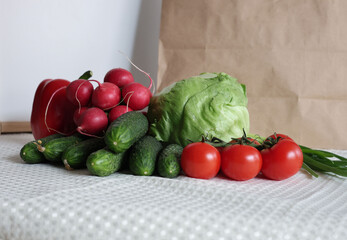 A colorful arrangement of fresh vegetables purchased at a local farmer’s market, including iceberg lettuce, radishes, cucumbers, tomatoes, and red bell peppers.