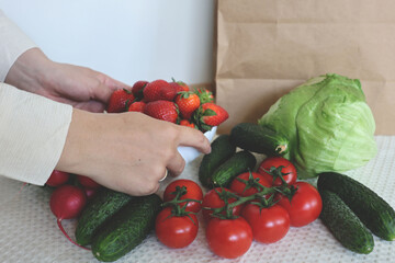 A close-up image showing hands arranging a bowl of ripe strawberries surrounded by fresh vegetables...