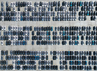 Aerial view of new cars stock at factory parking lot. Above view cars parked in a row. Automotive industry. Logistics business. Import or export new cars at warehouse. Big parking lot at port terminal