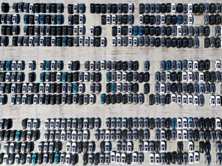 Aerial view of new cars stock at factory parking lot. Above view cars parked in a row. Automotive industry. Logistics business. Import or export new cars at warehouse. Big parking lot at port terminal