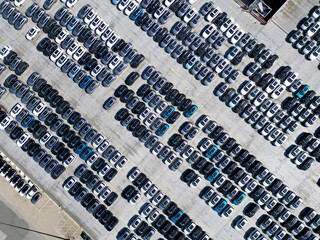 Aerial view of new cars stock at factory parking lot. Above view cars parked in a row. Automotive industry. Logistics business. Import or export new cars at warehouse. Big parking lot at port terminal