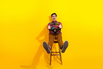 Cheerful young man sitting on a stool with a steering wheel against a yellow background, showcasing...