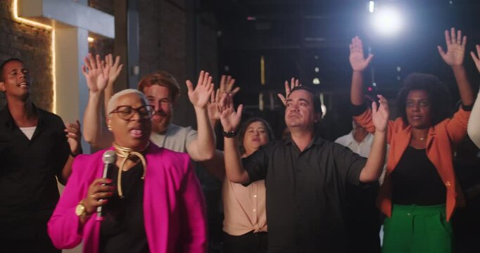 Woman leading heartfelt church worship, diverse congregation singing with hands raised, brick wall and glowing cross creating spiritual atmosphere