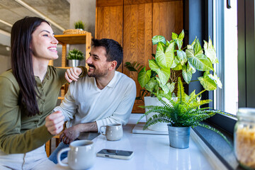 Happy couple spending time together, talking and smiling during coffee break in modern kitchen with...