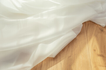 White transparent fabric on a background of light wood with sun rays.