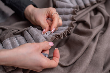 Women's hands in a close angle put hooks on the ribbon on the curtains. Brown curtains.
